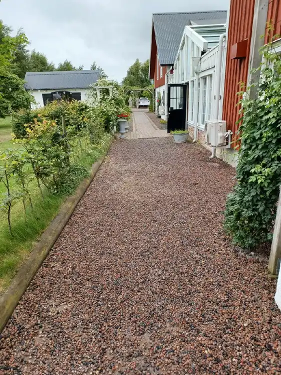 En grusad uppfart vid Hotell & Spa Lögnäs Gård. Gångvägar syns omgivna av grönska.