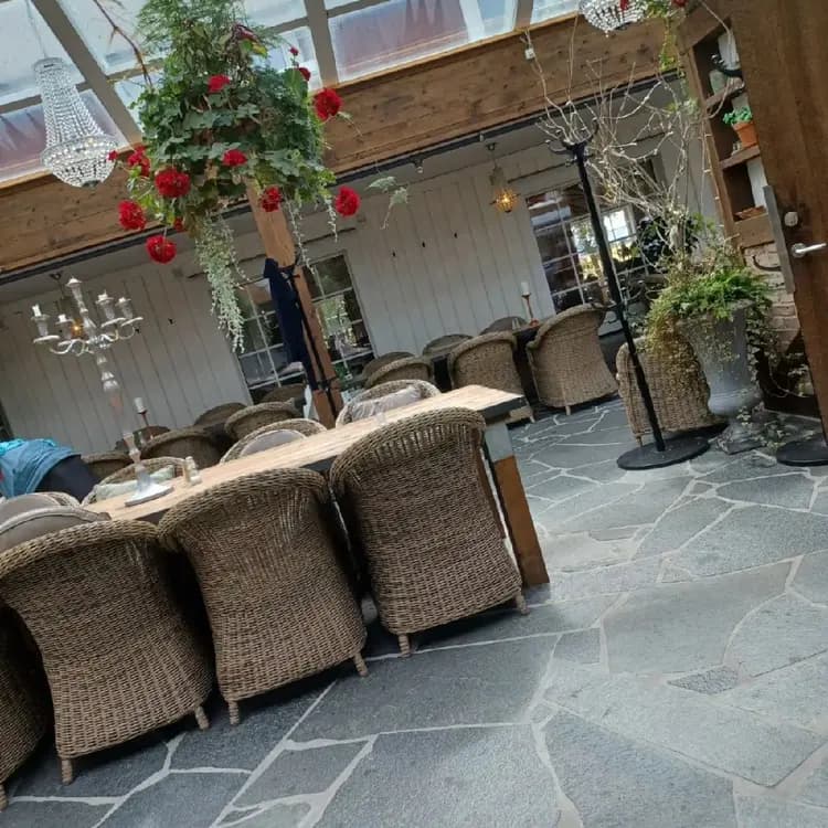 En solig innergård vid Hotell & Spa Lögnäs Gård med utplacerade blomkrukor, stolar och utebord i naturliga material på stengolv.