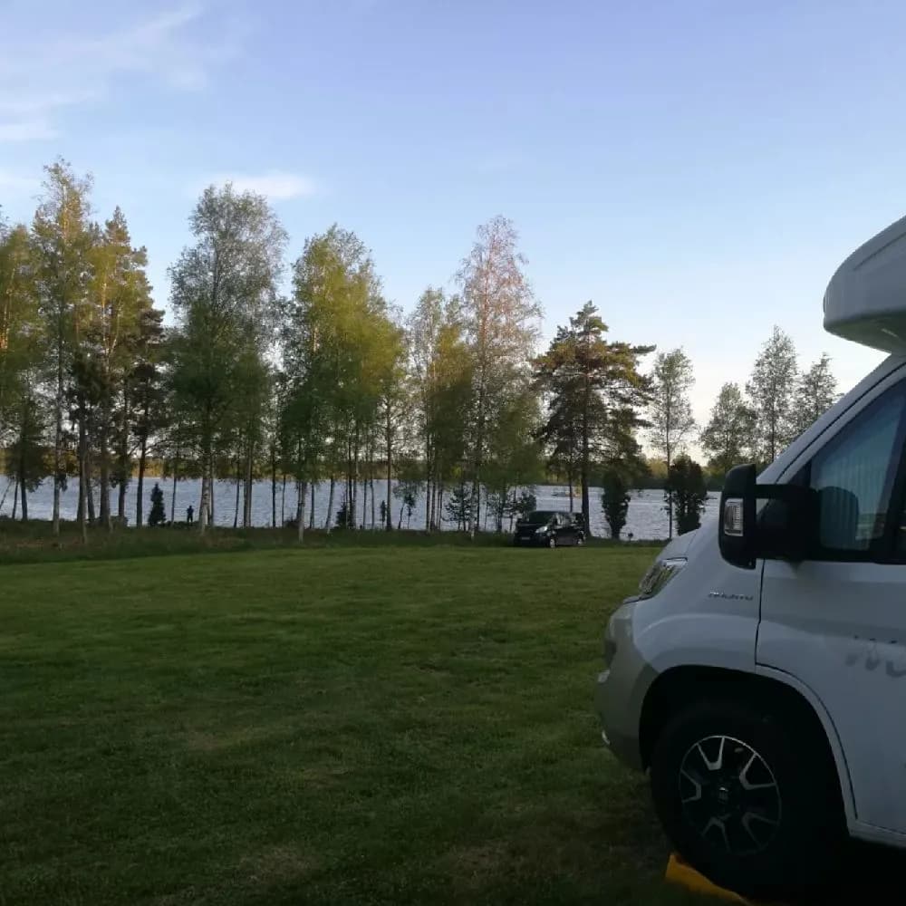 En bil parkerad på en gräsmatta framför Moarps B&B, som omges av skuggade träd. Bilen ser ut som en familjebil av lyxmodell.