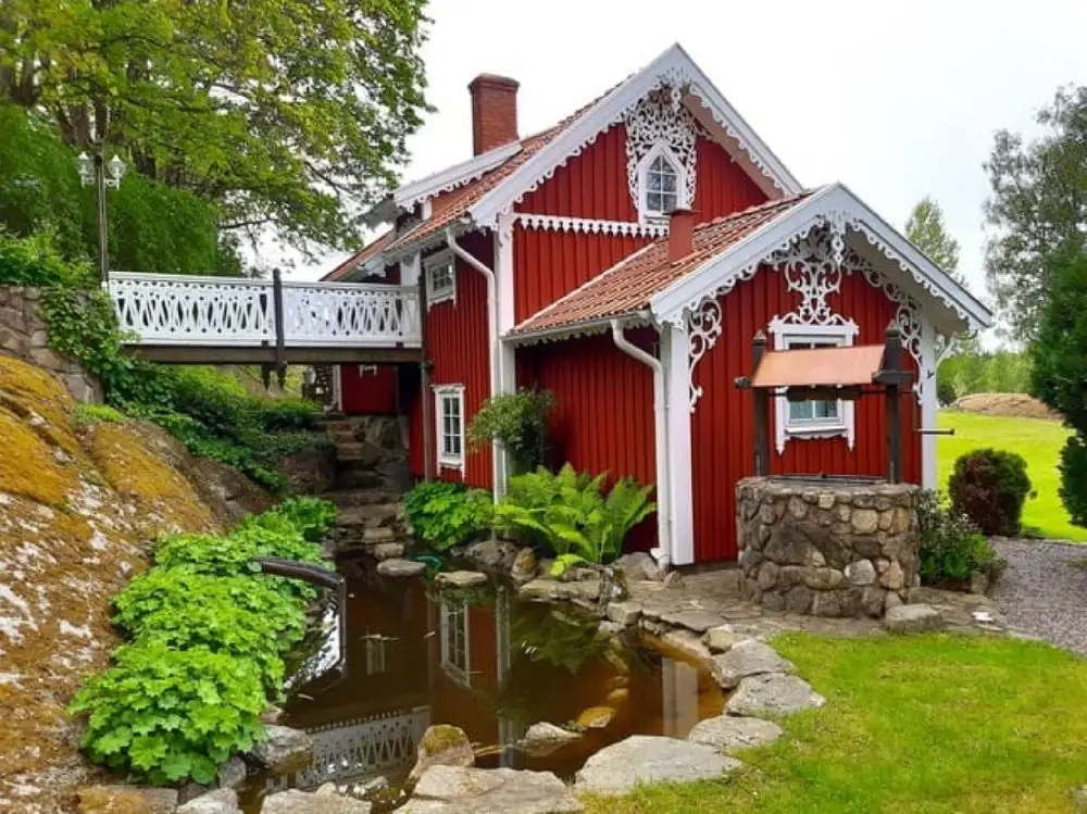 En gul stuga med vitt tak och blå dörr omgiven av grönskande växter och trädgård, visar en charmig och hemtrevlig atmosfär vid Moarps B&B.