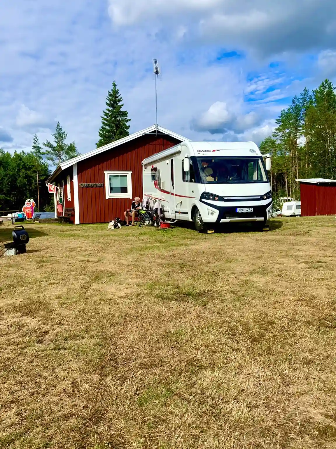 En husbil är parkerad på en naturnära campingplats vid Hoks naturcamping, omgiven av frodig grönska och träd.