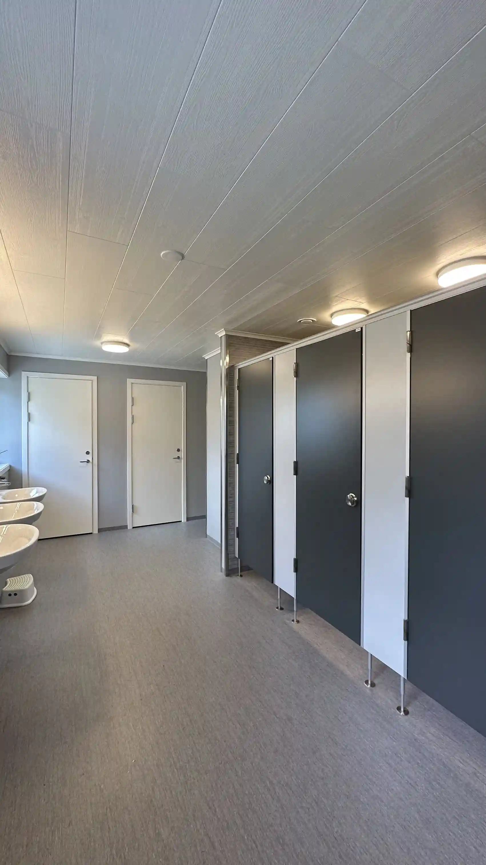 Interiör av ett modernt och enkelt rum med golvplattor, metalliska dörrar och takbelysning, typisk för Hoks naturcamping.