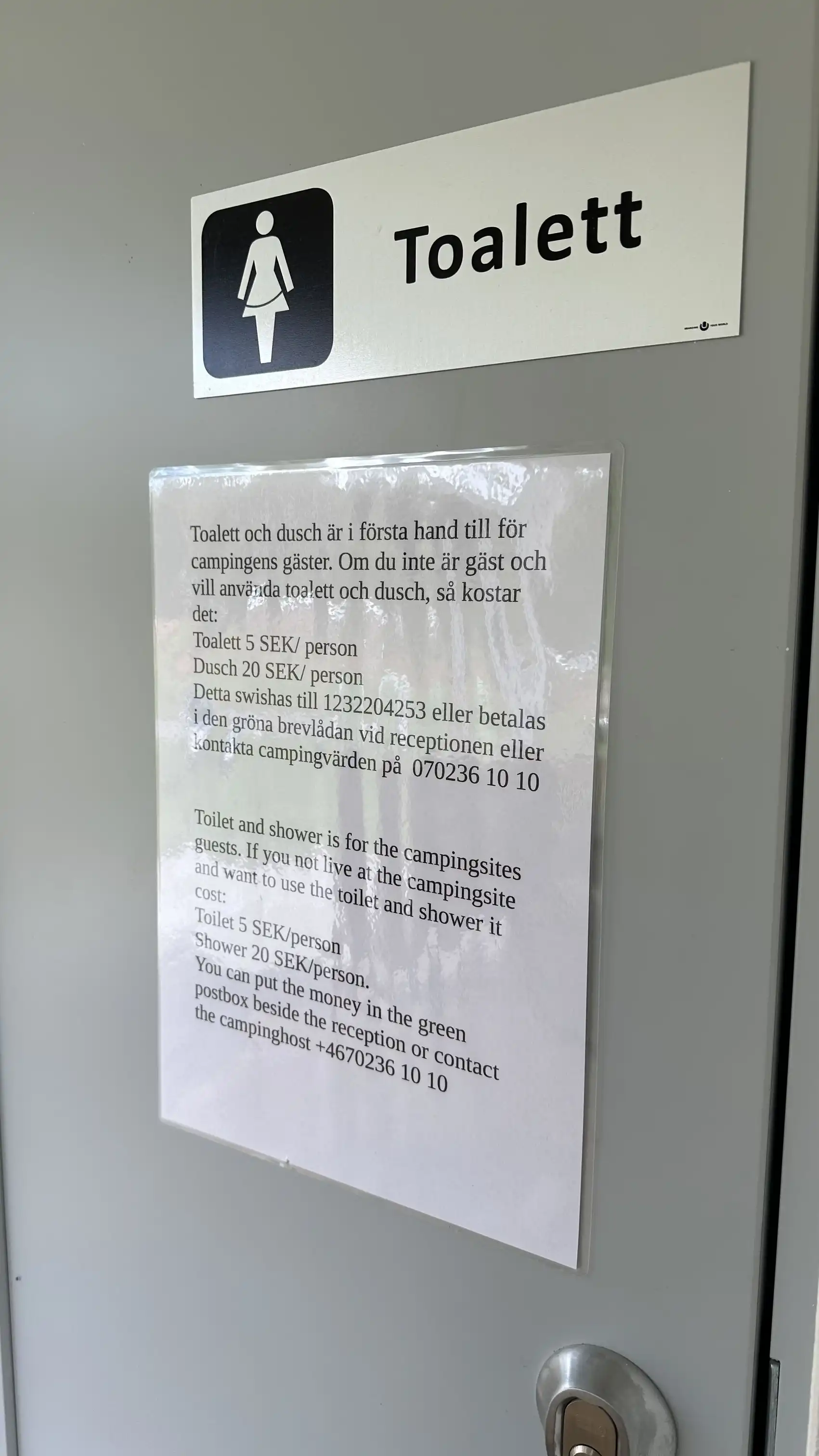 En grå aluminiumskylt med symboler och text visar vägen vid Hoks naturcamping.