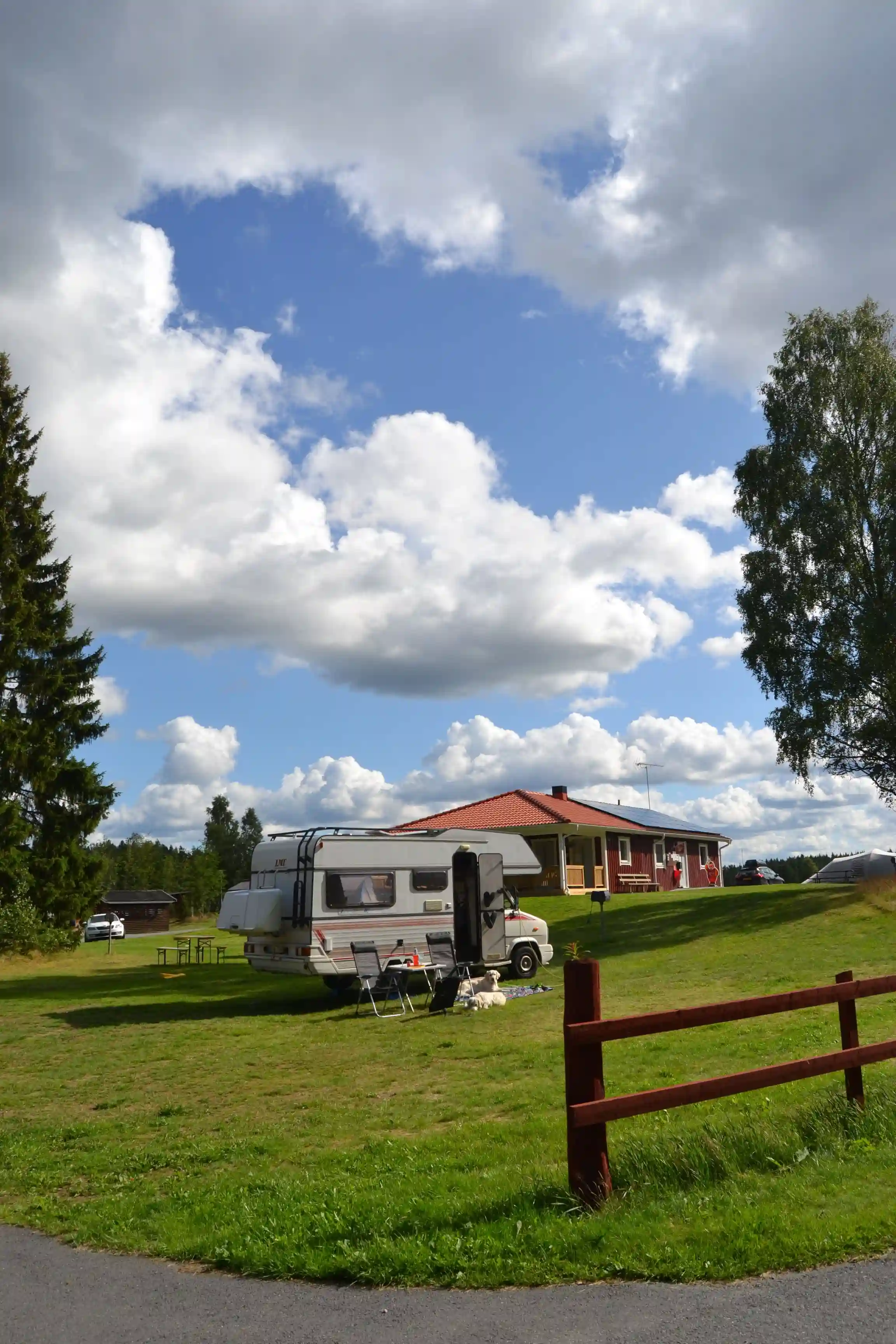 En vidsträckt äng vid Hoks naturcamping med gräs och några moln på himlen. En husbil står parkerad på gräset och skapar en idyllisk campingmiljö.