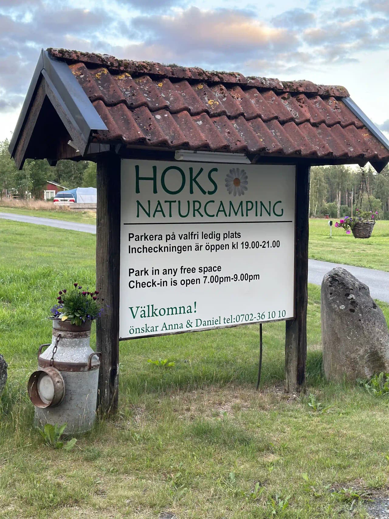 En vy över Hoks naturcamping med tält uppställda på en grön gräsmatta, omgivna av träd och parkmiljö. I bakgrunden syns små trädgårdsbyggnader som skapar en fridfull campingatmosfär.