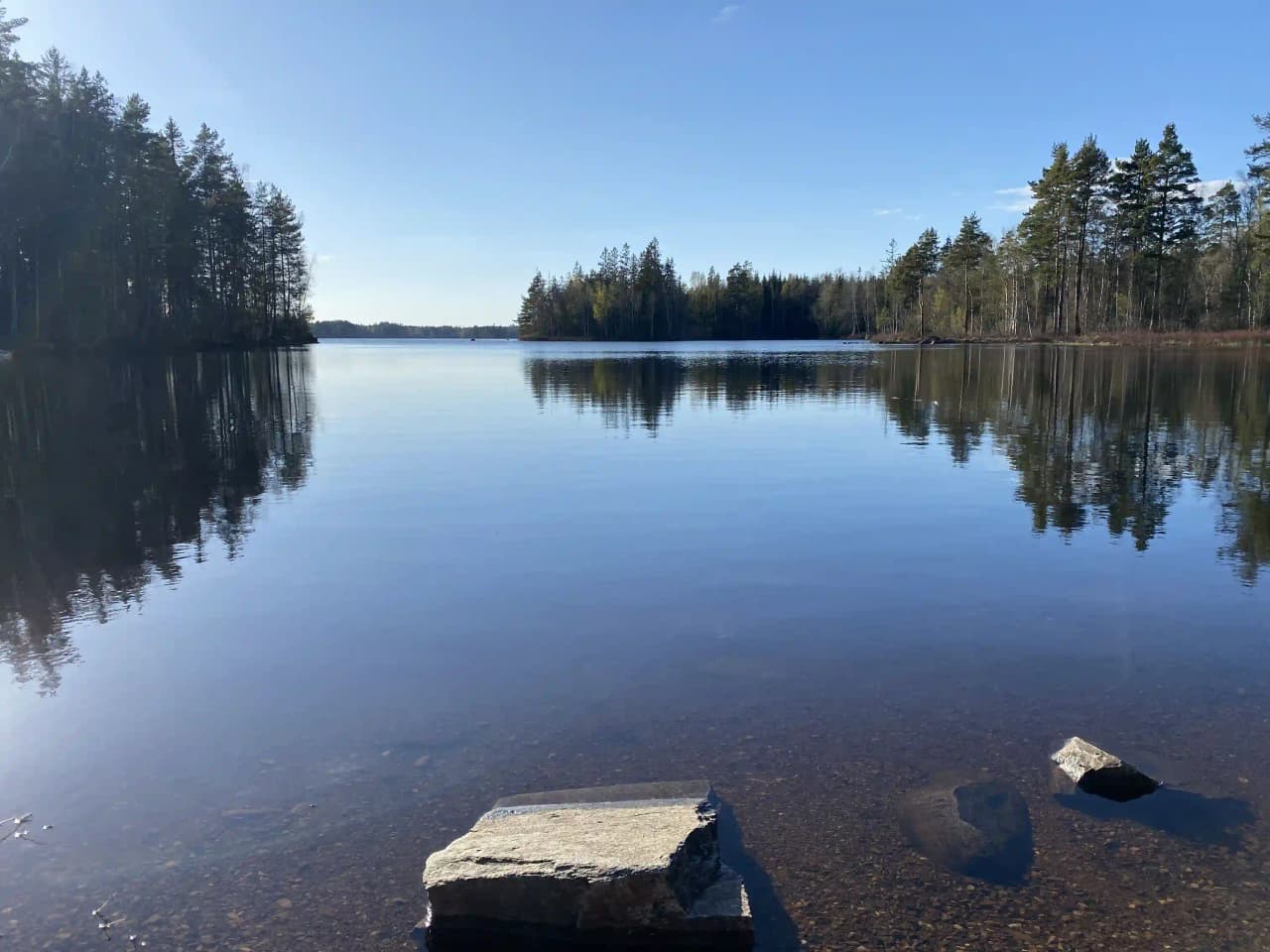 En naturskön vy över en stilla sjö vid Orrefors camping, med blått vatten som speglar den omgivande naturen.