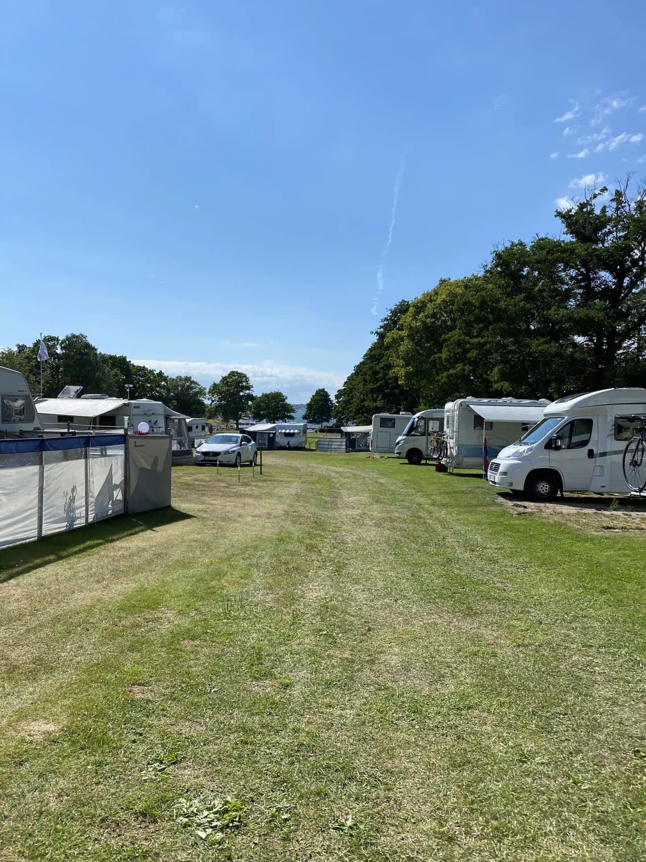 En campingplats vid Stenbräckagården Hägnan, med flera husbilar och husvagnar parkerade på ett öppet område under en himmel med vita moln.