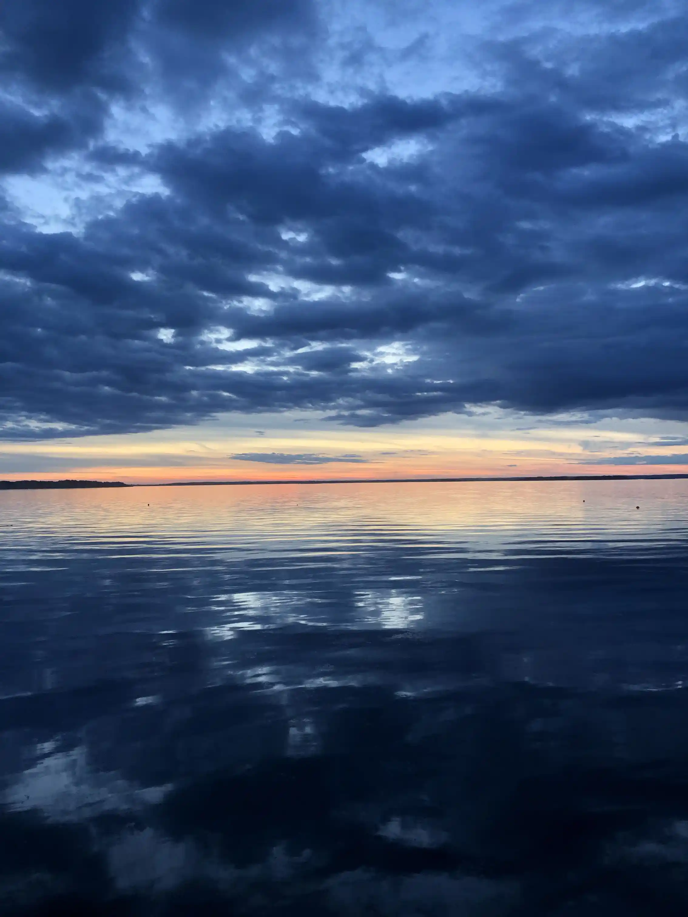 Bild av Stenbräckagården Hägnan med en vidsträckt himmel och moln i blåa nyanser. I förgrunden syns en glittrande vattenyta som sträcker sig mot horisonten, vilket skapar en lugn och fridfull atmosfär under dagtidens dämpade sken.