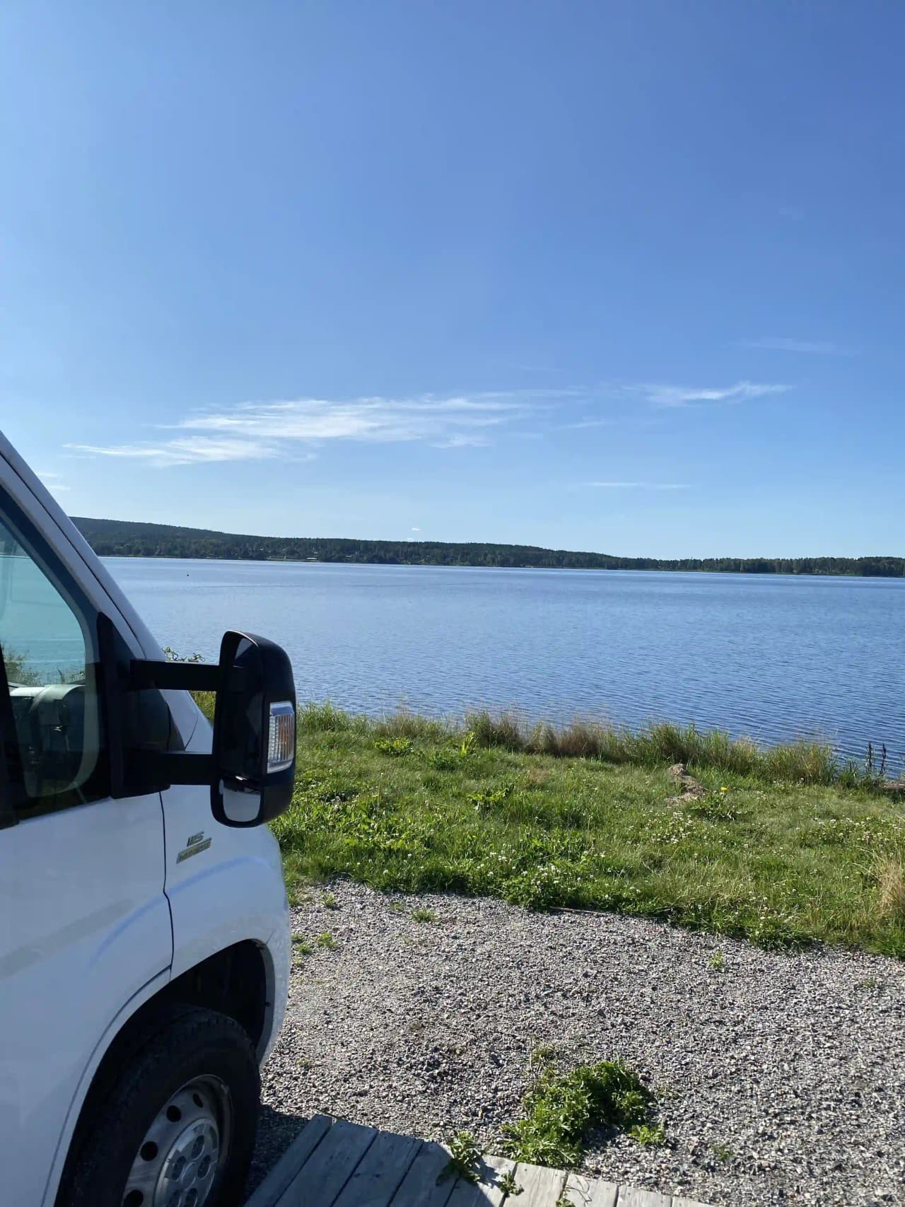 Bild av Arvika småbåtshamn: En väg längs hamnen med bilar parkerade, moln på himlen och vatten i bakgrunden.