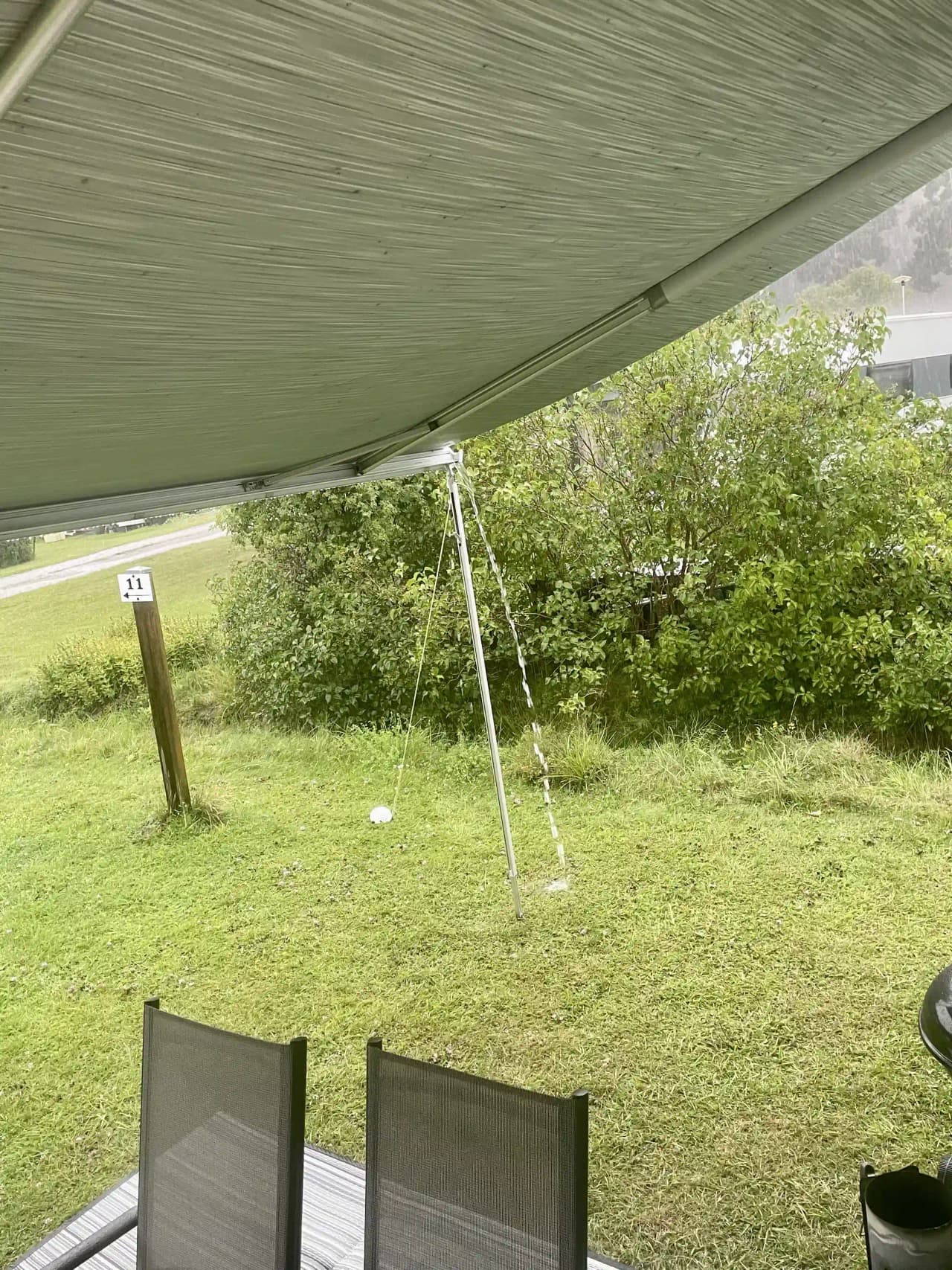 En grönskande campingplats med ett tält och solskydd i form av en markis. Det finns utemöbler på gräsmattan under skuggande träd vid Camp Nygård.