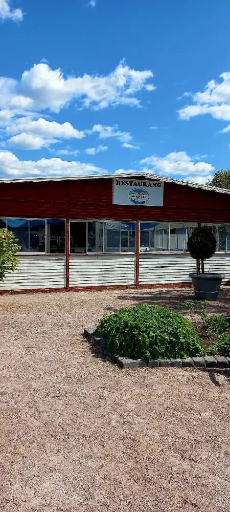 En skuggad uteplats vid Skantzö Bad & Camping med grönskande gräsmatta och trähusbebyggelse i bakgrunden.