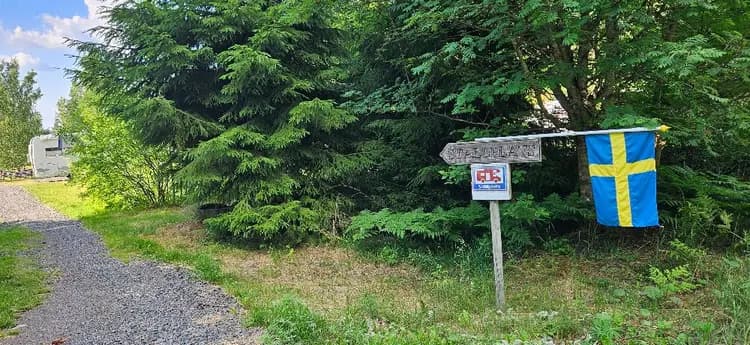 En skylt vid ingången till skogsområde vid Svennevads camping, omgiven av tät löv- och barrväxtlighet.