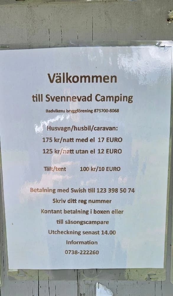 En grön campingplats med tält uppsatta på en gräsmatta, omgiven av lummig natur. Skyddande presenningar spända över några av tälten. Perfekt för friluftsliv och avkoppling.