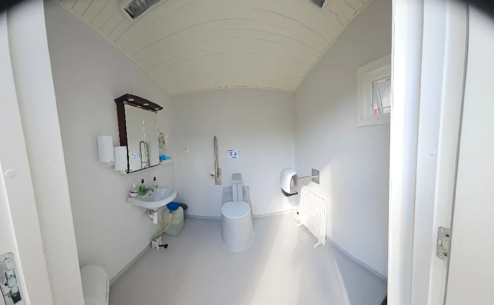 Bild av ett modernt badrum på Svennevads camping. Rummet har ljusa väggar och ett kaklat golv. Det finns en stilren vit handfat med en spegel ovanför, samt en dusch med glasdörrar. Insidan ger ett fräscht och ombonat intryck med enkel men smakfull design.