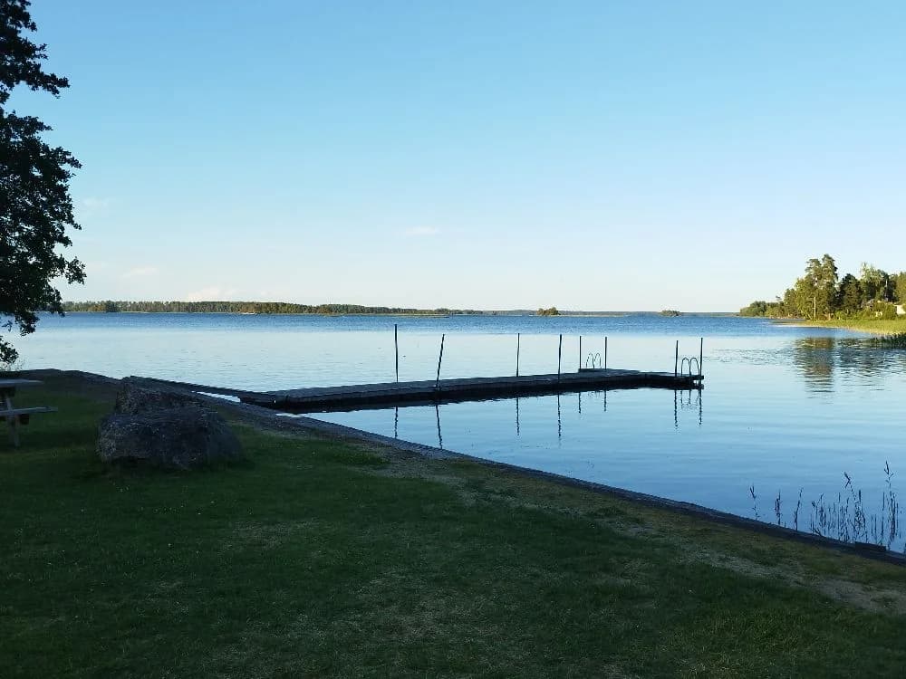 En vy över Svennevads camping med en blåsjö, omgiven av grönska och en brygga som sträcker sig ut i vattnet.