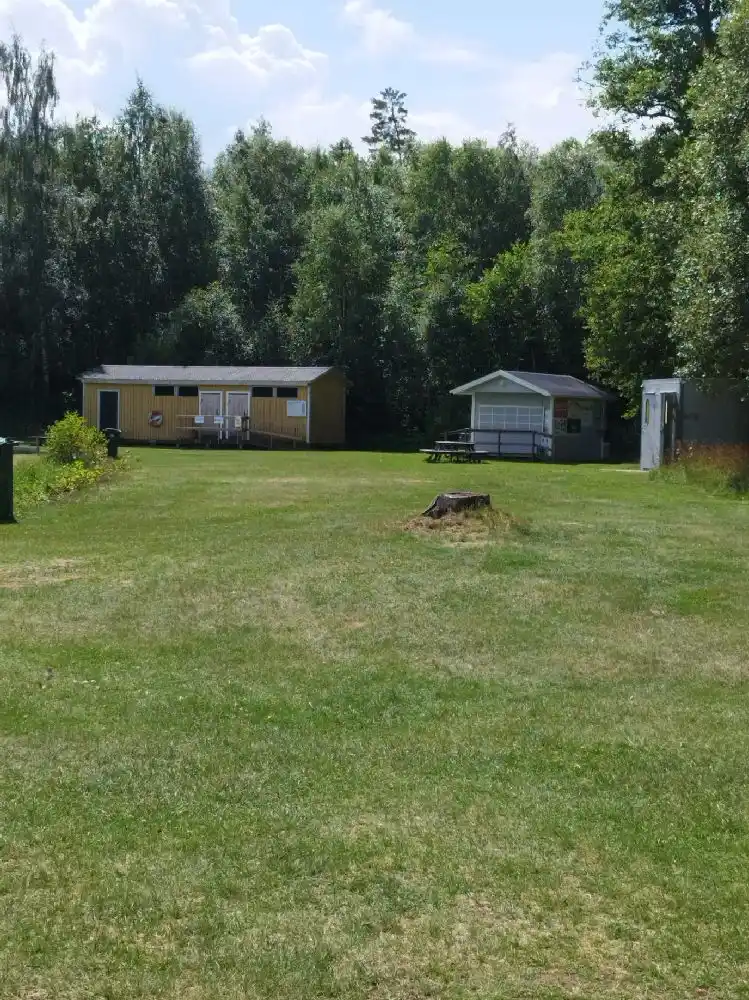 En grönskande äng med gräs och träd vid Svennevads camping, med en stuga i bakgrunden och lantlig miljö.