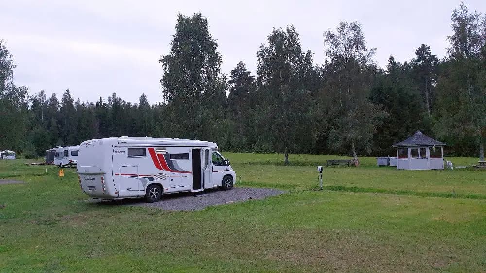Ett campingområde med husvagnar och tält uppställda på en grön gräsmatta omgiven av träd, perfekt för en avkopplande vistelse i naturen.