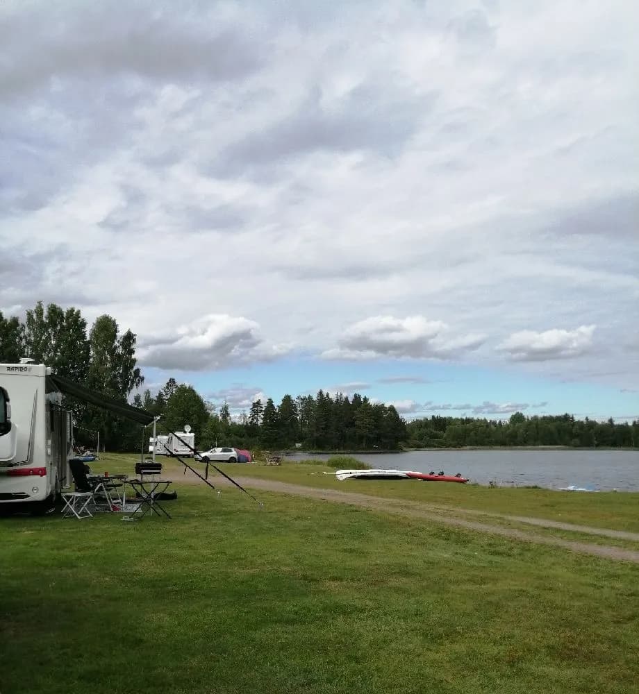 En vy över Steiners Camping & Lodge visar en vidsträckt gräsmatta under en delvis molnig himmel, med båtar och fritidsutrustning i närheten, omgiven av en öppen, naturskön miljö.