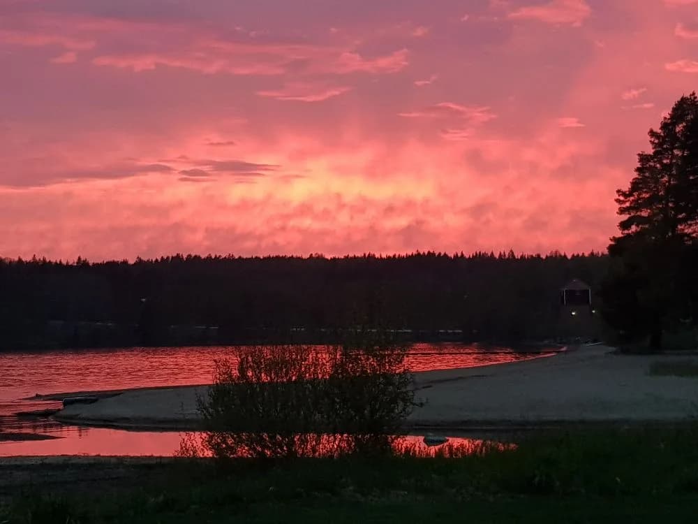 En fridfull vy över Ekeby Camping vid solnedgången, där himlen skiftar i orange och rödtoner mot horisonten.