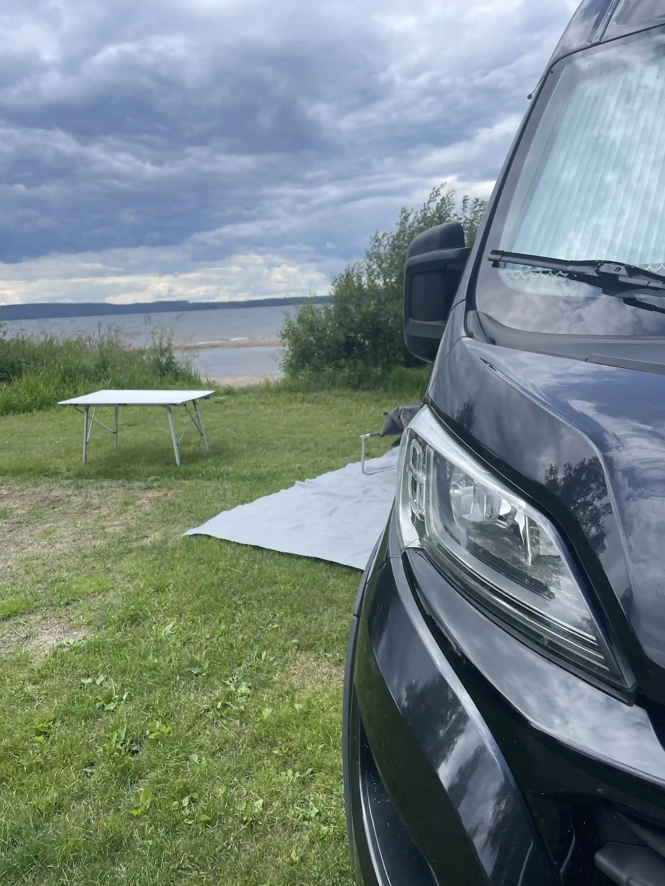 En kompakt minibuss står parkerad vid Ekeby Camping, omgiven av grönt gräs och skog i bakgrunden.