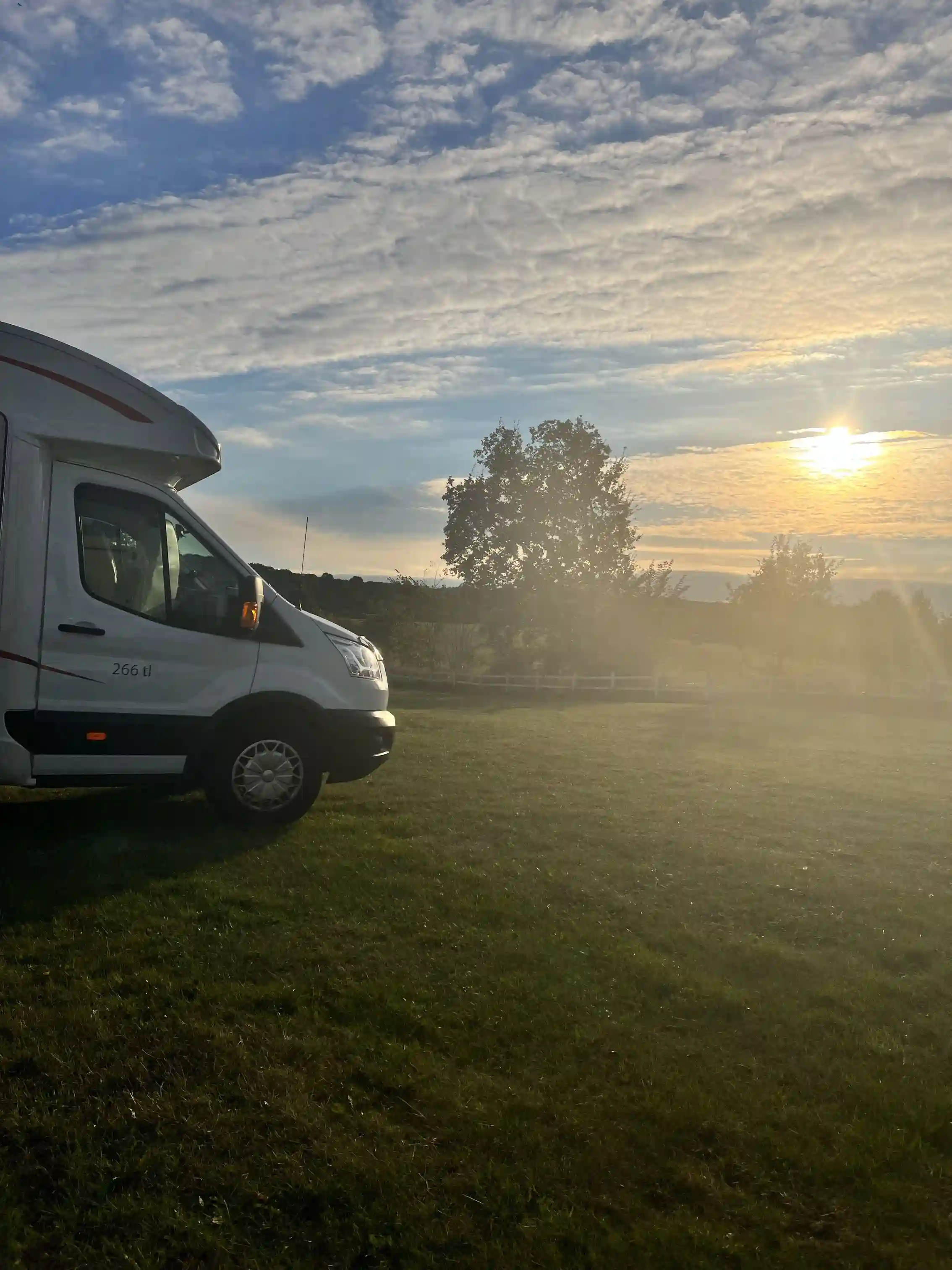 En campingplats vid ängdala på Österlen i skymningen med husbilar uppställda under en molnig himmel. Solnedgången skapar ett varmt ljus över området.
