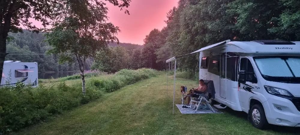 En husbil och en husvagn parkerade på Värnäs camping, omgivna av tält och grönskande natur.