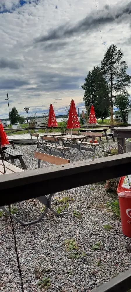 En solig dag vid Borgaruddens havsbad och familjecamping. Bilden visar utomhusmöbler bestående av picknickbord och bänkar, omgivna av molnig himmel.