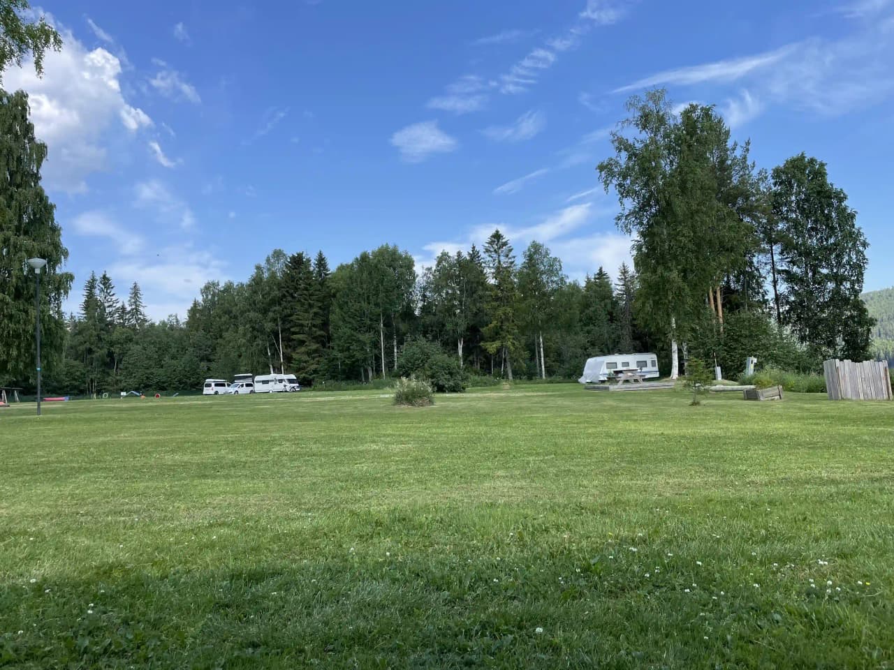 En grön campingplats med frodig gräsmatta och omgivande träd vid Hammarstrands camping, under en molnig himmel.