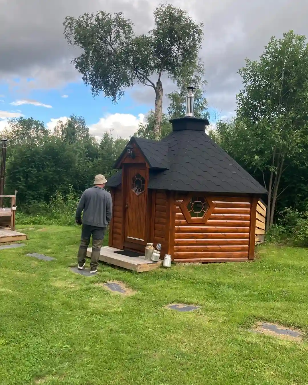En timmerstuga på Hammarstrands camping omgiven av grönska, med träpaneler och ett snedtak.