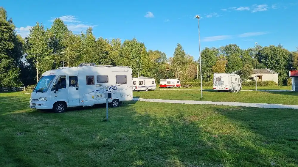 En campingplats med flera husbilar och husvagnar parkerade på grönskande gräs.