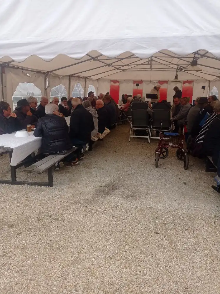 En campingplats med tält och ett uppställt soltak. Under taket finns utemöbler inklusive stolar och ett bord, omgivna av träd och grönska.