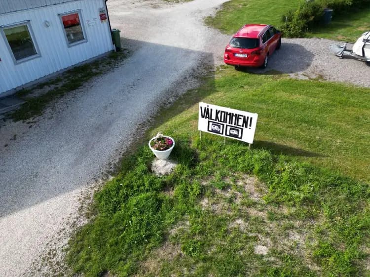 En översiktsbild av Kerstins camping visar en grönskande campingplats med välskötta gräsmattor och en infart. En skylt markerar campingområdet.