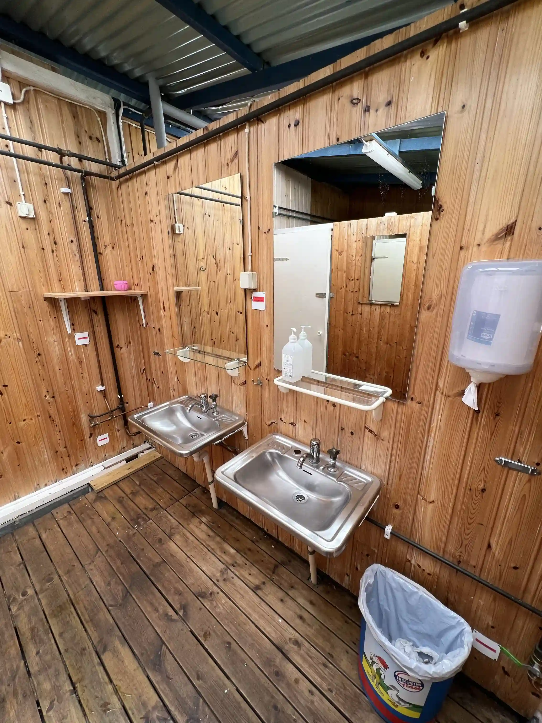 Alt-text: Interiörbild av en byggnad på Björkenäs camping med trä-inredning, inklusive ett golv och väggar av trä och plywood. Städad och välvårdad miljö med inslag av metallrör.