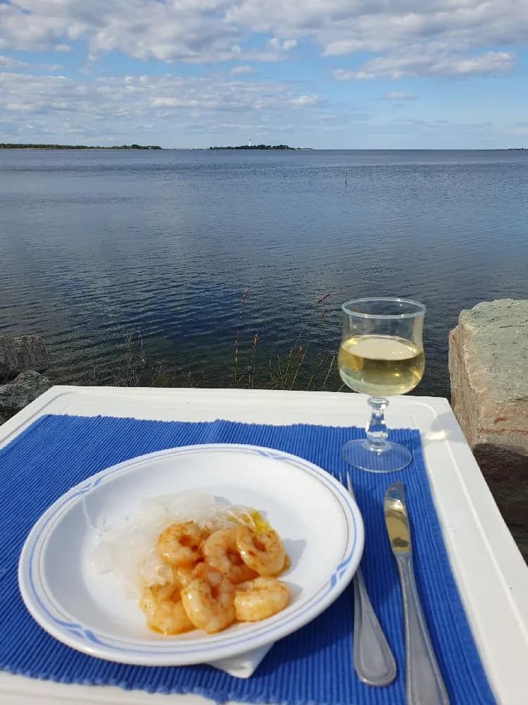 En utsikt över ett dukat bord med tallrikar, glas och bestick vid Böda hamns camping. I bakgrunden syns havet.