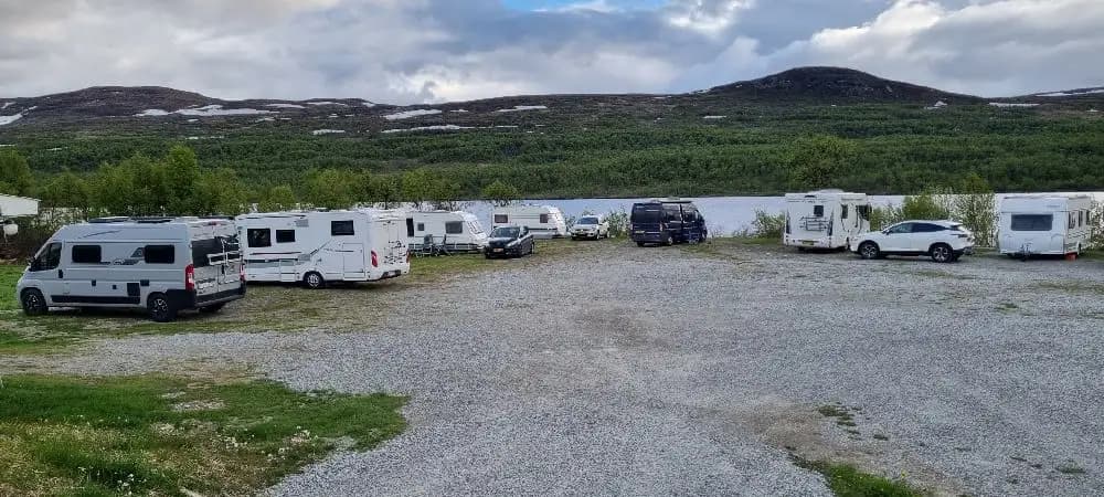 En campingplats med parkerade husbilar och husvagnar, omgiven av en naturskön miljö och närhet till berg och sjöar, typisk för Lake District.