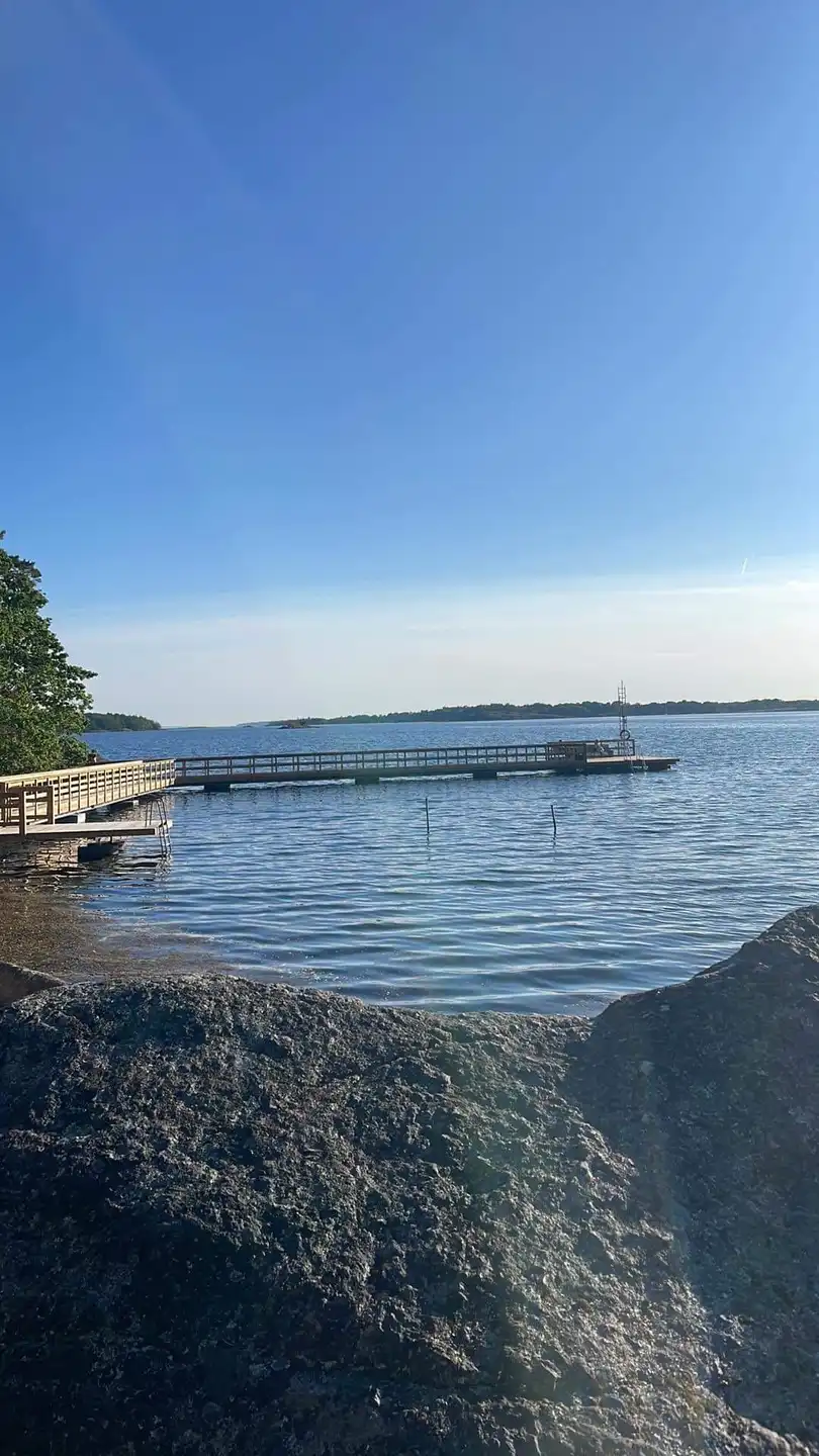 En solig dag vid Järnaviks camping med blå himmel och stilla vatten som breder ut sig mot horisonten, omgiven av kustlinjer och molnformationer.