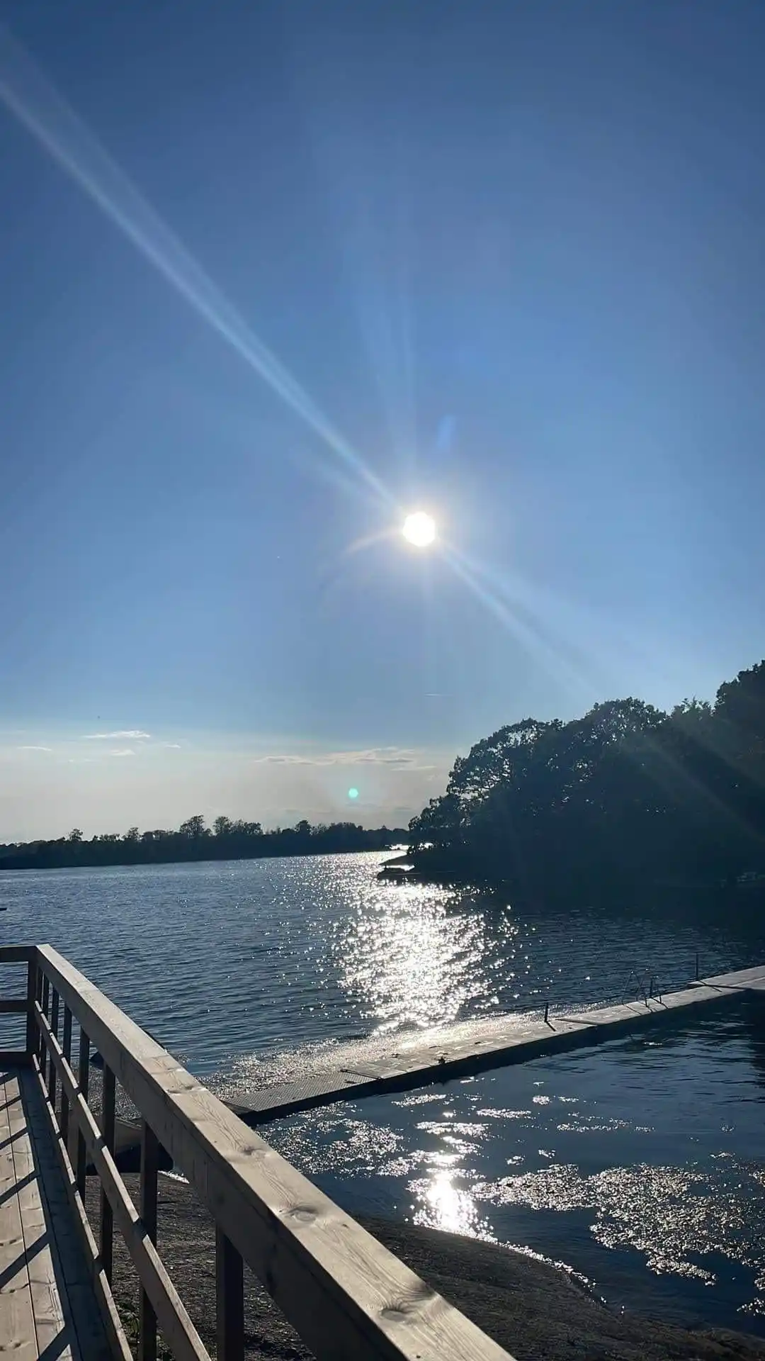 En vidsträckt vy över en klarblå sjö vid Järnaviks camping med en horisontlinje där himmel möter vatten och solen reflekteras på vattenytan.