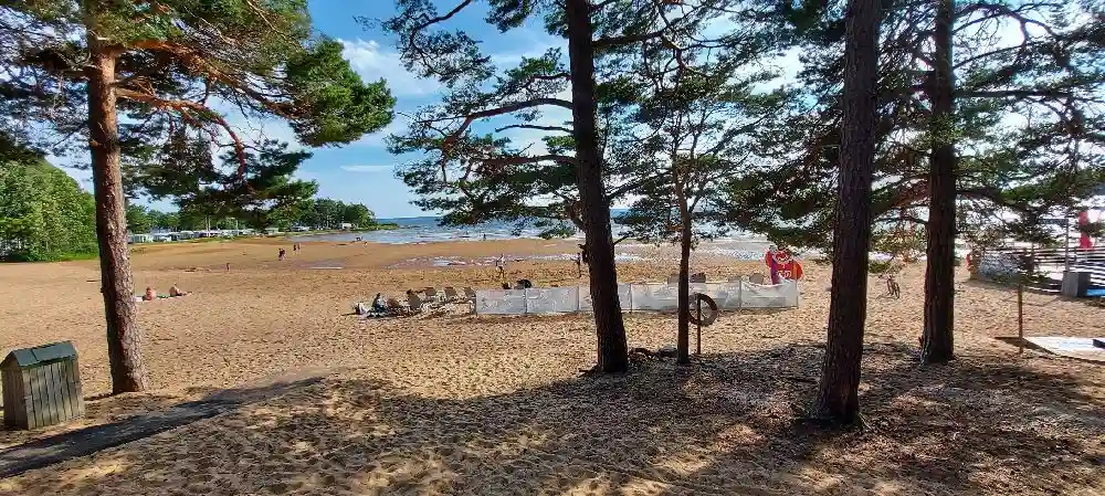 En somrig strand vid Bomstadbaden camping med vidsträckt himmel, sandig kust och glittrande hav i bakgrunden.