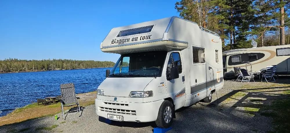 Bild av en parkeringsplats för husbilar vid Uvaparken. Flera husbilar står uppradade med synliga komponenter som stötfångare, sidospeglar och registreringsskyltar. Området är förberett för camping med olika typer av campingfordon.