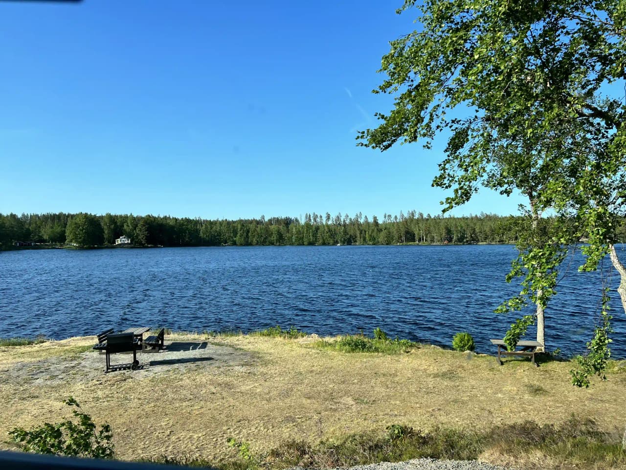 En naturskön sjö med blått vatten och grönskande strandkant vid Uvaparken Ställplats.