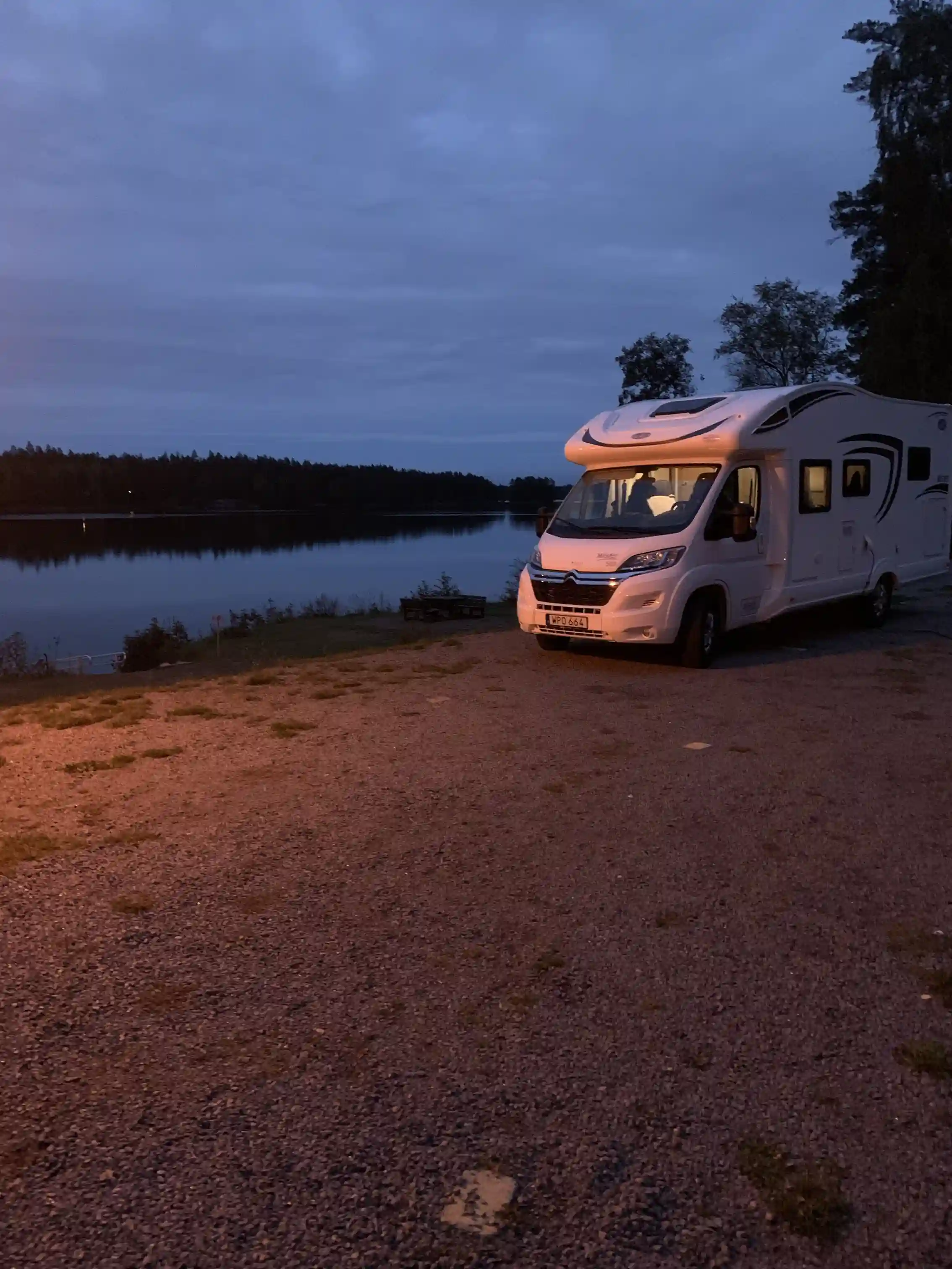 Bild av en husbil parkerad vid Uvaparken ställplats under skymningen, med en vacker solnedgång i bakgrunden.