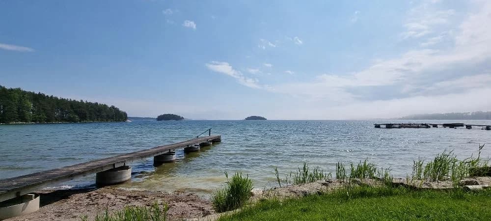 En vacker sjö vid Jogersö Eco Camping, med klart vatten som omges av grönskande strandkanter och en vidsträckt horisont.