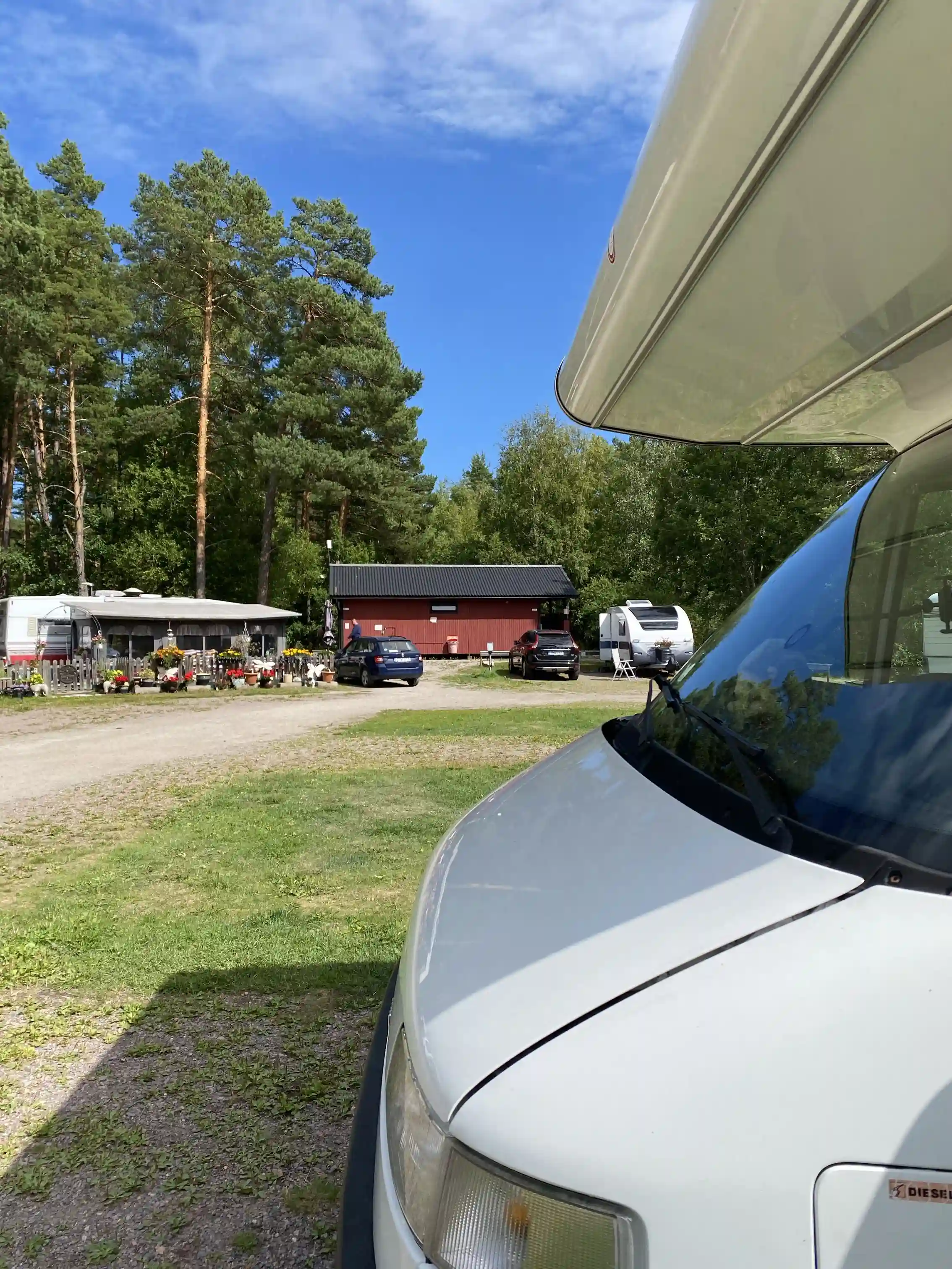 En bil parkerad vid Strandstuvikens havsbad & camping, omgiven av tallskog och sanddyner i bakgrunden.