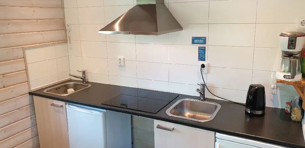 Bild av ett kök på Långsjön Stugor & Camping, med träinredning och parkettgolv. Köket är utrustat med vitvaror som kylskåp och spis, samt en diskbänk och bänkskivor. Interiören är ljus och rustik, vilket ger en hemtrevlig atmosfär.