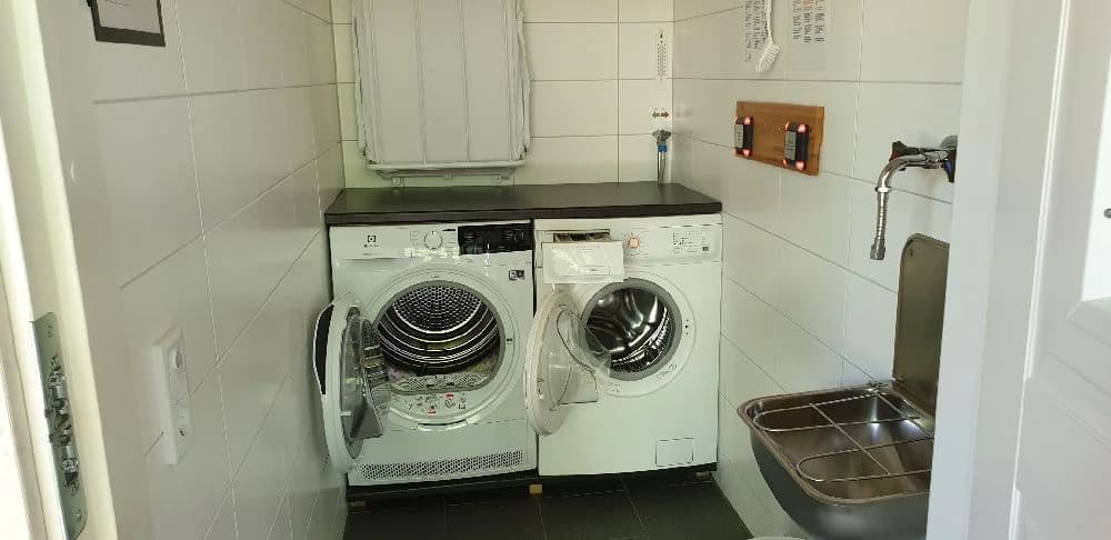 En tvättstuga med tvättmaskin och torktumlare, inredd med olika tvättprodukter och förnödenheter för klädtvätt, vilket erbjuder bekvämligheter för besökare på Långsjön Stugor & Camping.