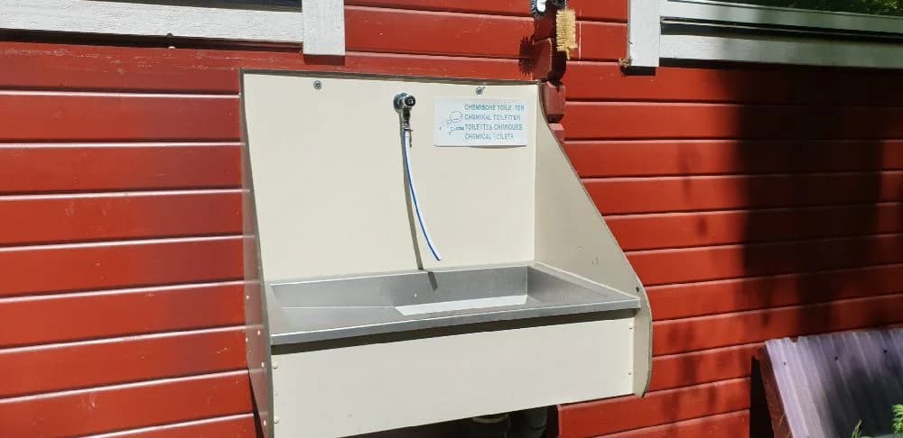 En trästuga vid Långsjön Stugor & Camping, omgiven av grönska. Träpanelerna har en naturlig träbets som smälter in i den natursköna miljön.