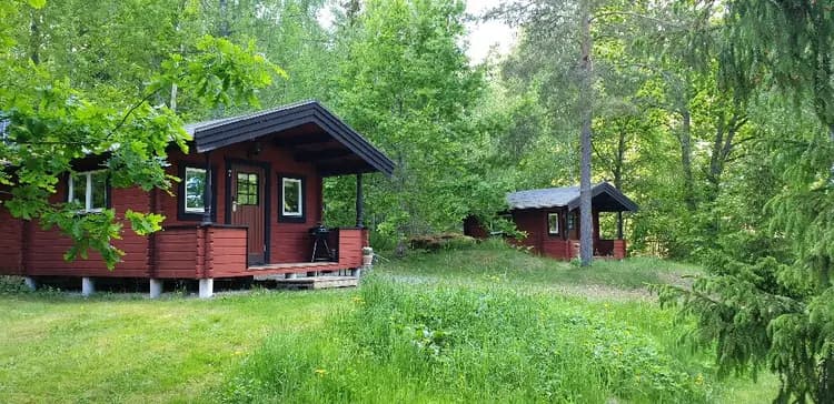 Alt-text: En lantlig stuga i trä omgiven av skog och trädgårdsbyggnader vid Långsjön Stugor & Camping.