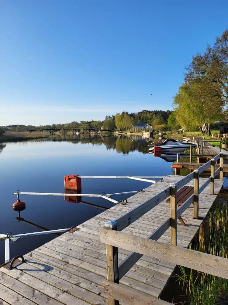 En sjö med klart blått vatten och en brygga som sträcker sig från stranden. Vattnet reflekterar himlen och omgivande landskap.