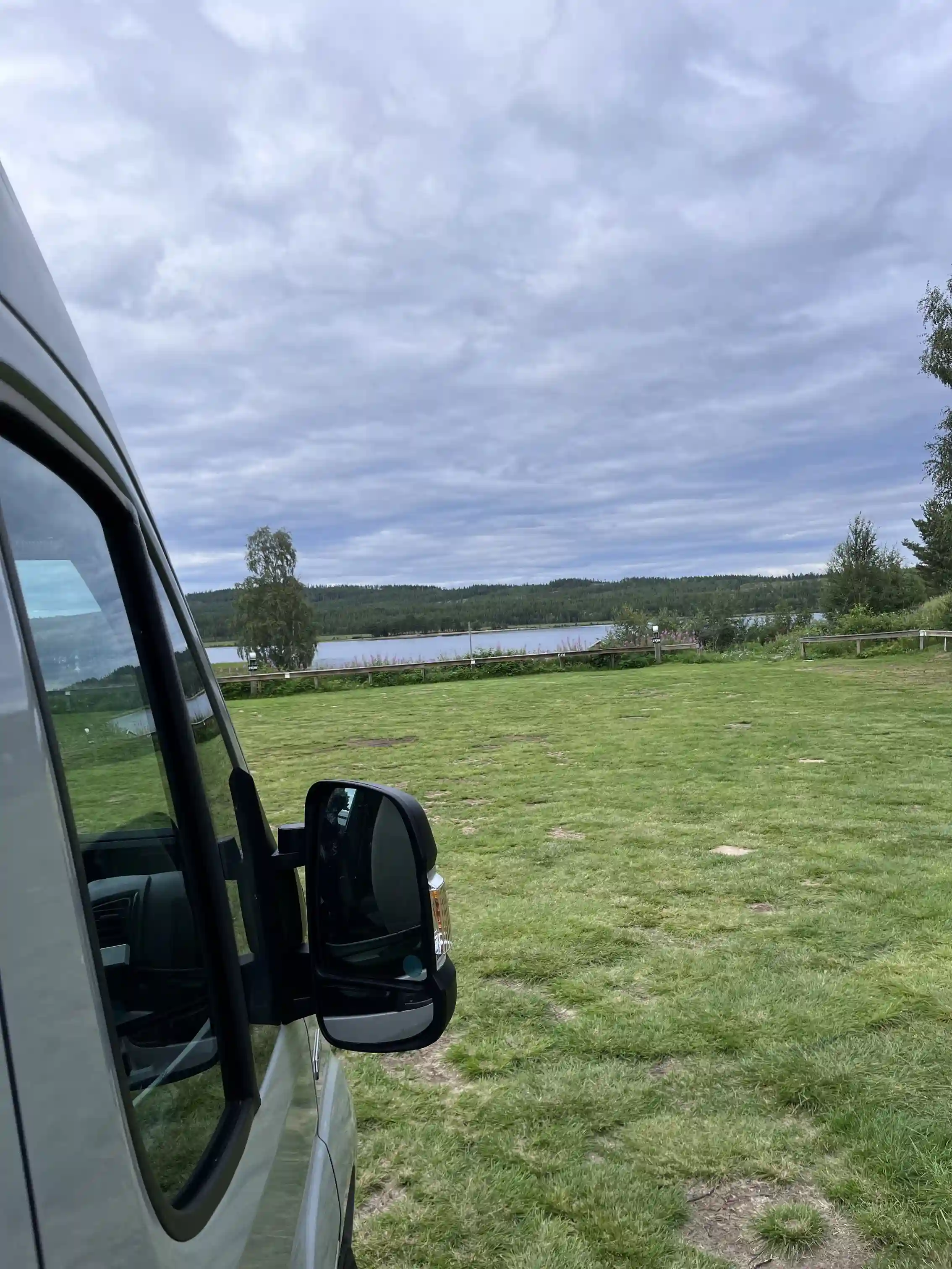 En campingplats i naturskön miljö med ett fordon parkerat på en gräsmatta under en molnig himmel.
