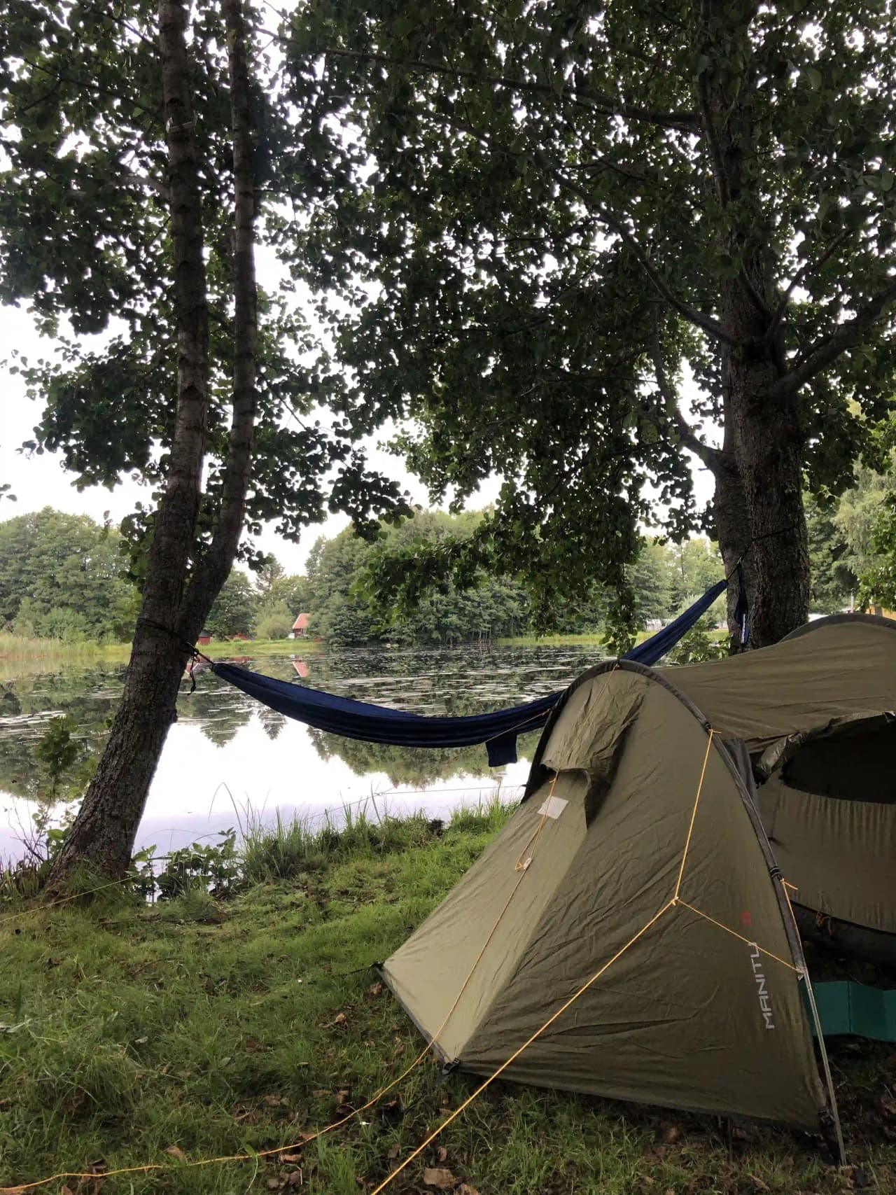 En campingplats med tält och fritidsutrustning under ett solskydd, omgiven av grönska. Perfekt för friluftsliv och semester på Simbadets camping.
